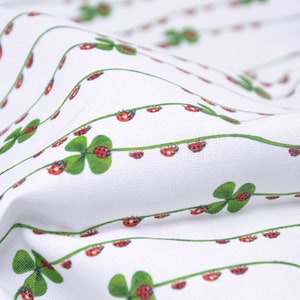 May include: White fabric with a repeating pattern of green four-leaf clovers and red ladybugs. The clovers are connected by thin green stems.