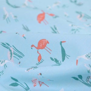 Pode incluir: Um tecido azul claro com um padrão repetido de flamingos cor-de-rosa e pássaros brancos. Os pássaros são representados em um design simples e estilizado, enquanto os flamingos são mais detalhados. O tecido tem uma textura macia.