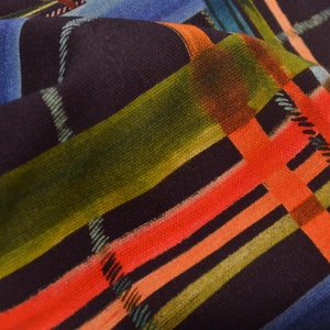 Könnte beinhalten: Nahaufnahme eines Stoffes mit einem bunten Karomuster. Der Stoff ist aus einem weichen, gewebten Material gefertigt und hat einen Mix aus roten, orangen, grünen, blauen und schwarzen Streifen.