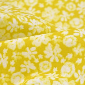 Pode incluir: Tecido amarelo com um padrão floral branco. O tecido tem uma superfície macia e texturizada.