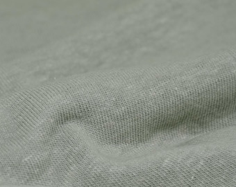 Könnte beinhalten: Nahaufnahme eines weichen, hellgrünen Stoffes mit einer strukturierten Webart. Der Stoff ist zerknittert und hat ein natürliches, leinenartiges Aussehen.