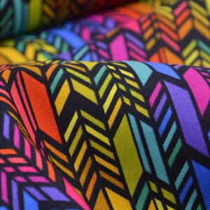 Könnte beinhalten: Nahaufnahme eines Stoffes mit einem sich wiederholenden geometrischen Muster. Das Design zeigt farbenfrohe, pfeilartige Formen in Rosa, Orange, Gelb, Grün, Blau und Lila auf schwarzem Hintergrund. Der Stoff ist gefaltet und zeigt seine Textur.