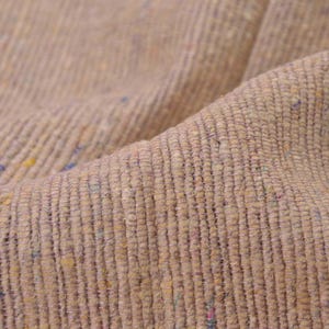 May include: Close-up of a textured fabric in shades of tan and beige. The weave is visible with vertical lines and small flecks of color, including blue, yellow, and pink, adding visual interest to the textile.