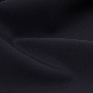 May include: Close-up of a smooth, dark blue fabric with a subtle sheen. The fabric is draped and folded, creating soft curves and shadows.