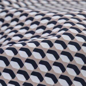Peut inclure: Gros plan sur un tissu beige avec un motif géométrique répétitif de formes noires et blanches. Le tissu a une texture subtile et un léger brillant.