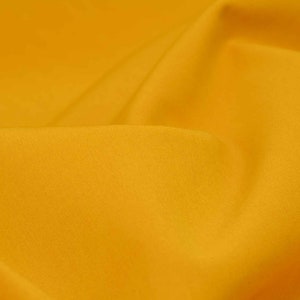 Pode incluir: Um close-up de um tecido amarelo liso com uma textura suave e sutil. O tecido está dobrado e drapeado, criando uma curva suave.