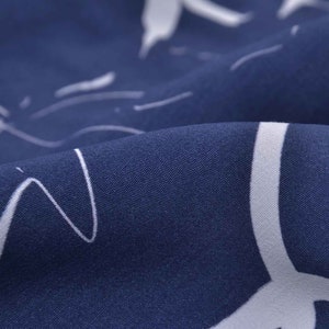 May include: Close-up of a navy blue fabric with a white abstract pattern. The fabric has a smooth, textured surface.