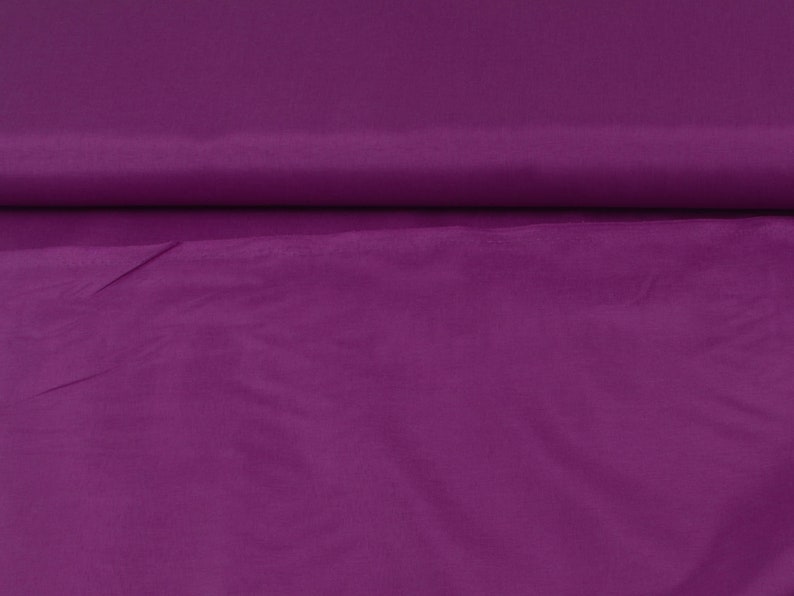 May include: A close-up of a smooth, solid purple fabric. The fabric has a slight sheen and is folded in half.