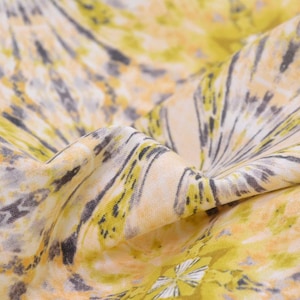 Pode incluir: Close-up de um tecido branco com um padrão tie-dye amarelo, laranja e cinza. O tecido é macio e tem um brilho sutil.