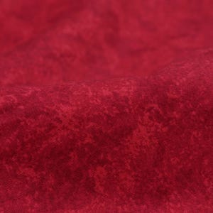 Può includere: Primo piano di un tessuto rosso strutturato con un motivo maculato. Il tessuto ha un aspetto leggermente stropicciato, con sottili variazioni di colore e consistenza. Il materiale sembra morbido e flessibile, adatto per abbigliamento o arredamento.