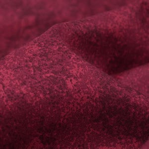 Op de afbeelding: Close-up van een dieprode stof met een subtiel gespikkeld patroon. De stof voelt zacht en textuurrijk aan.
