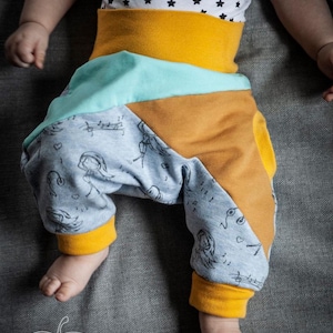 May include: Baby clothing set featuring a white top with black star patterns and colorful pants. The pants have a mustard yellow waistband and cuffs, with a light blue and orange patchwork design. The pants also have a gray pattern with musical notes and figures.