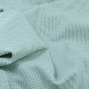May include: A close-up of a light blue waffle knit fabric. The fabric is soft and textured, with a subtle sheen.