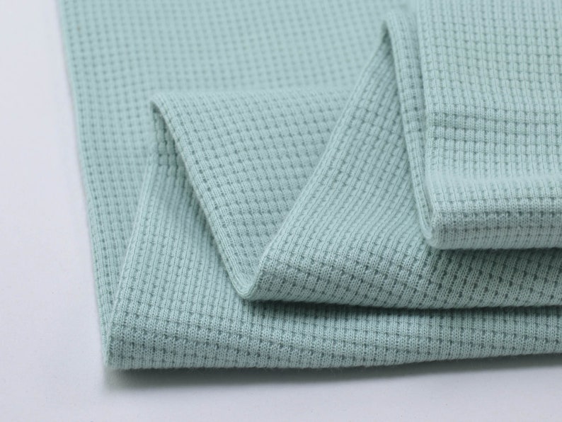 May include: A close-up of a light blue waffle knit fabric. The fabric is folded in half and the texture of the knit is visible.