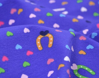 May include: Purple fabric with a repeating pattern of colorful hearts and orange horseshoes.