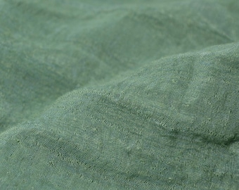 May include: Close-up of a green fabric with a textured woven pattern. The fabric has a soft, slightly wrinkled appearance.