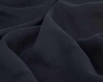 May include: A close-up of a dark blue fabric with a smooth, textured surface. The fabric is folded and draped, creating soft folds and curves.