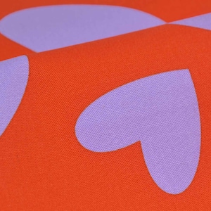 May include: Close-up of a fabric with a repeating pattern of purple hearts on a bright orange background.
