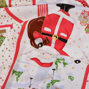 Peut inclure: Tissu de Noël festif avec le Père Noël, des rennes et des cadeaux. Le tissu blanc présente des bordures et des accents rouges, décoré d'étoiles et de sapins de Noël. L'illustration du Père Noël est détaillée avec un costume rouge et une barbe blanche.