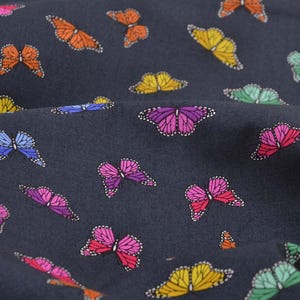 Könnte beinhalten: Dunkelblauer Stoff mit einem sich wiederholenden Muster aus bunten Schmetterlingen. Die Schmetterlinge sind in den Farbtönen Orange, Gelb, Rosa, Lila, Blau und Grün gehalten und mit weißen Details versehen. Der Stoff hat eine leicht strukturierte Optik.