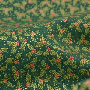 以下が含まれることがあります： 緑色の生地のクローズアップ。ヒイラギの葉と赤い実の繰り返し模様。葉は金色の縁取りで、小さな白い点が表面に散らばっています。クリスマスのクラフトに最適です。