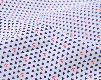 Op de afbeelding: Witte stof met een herhalend patroon van kleine blauwe hartjes en rode ankers.