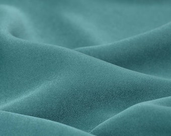 May include: Close-up of a soft, teal fabric with a smooth, slightly textured surface. The fabric is draped in folds, creating a gentle, flowing effect.