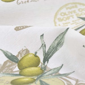 Pode incluir: Tecido branco com um padrão repetido de ramos de oliveira, azeitonas e um rótulo que diz "Pure Olive Oil Soft Soap".