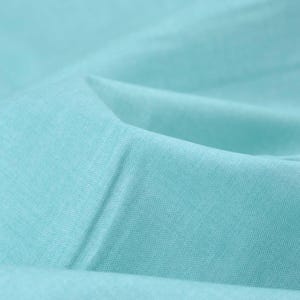 Puede incluir: Primer plano de una tela suave de color azul claro con una textura lisa. La tela está doblada y drapeada, creando una suave ola.