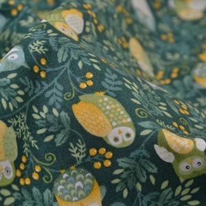 May include: Close-up of fabric featuring a repeating pattern of owls, leaves, and berries. The owls are in shades of yellow, green, and white, set against a dark teal background. The fabric has a soft, textured appearance.