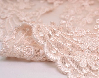 May include: Close-up of delicate, pale pink lace fabric with a floral pattern. The lace has a soft, flowing texture and a delicate, feminine look.