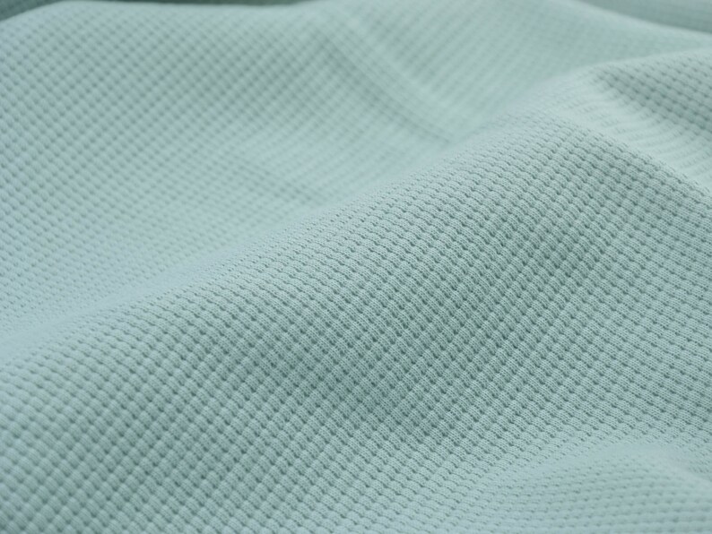 May include: A close-up of a light blue textured fabric. The fabric has a subtle waffle weave pattern.