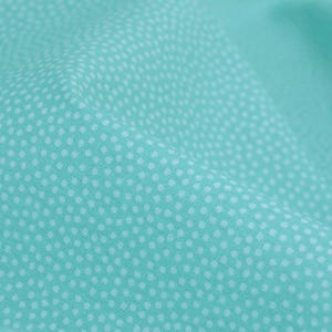 Puede incluir: Una tela turquesa con un patrón de lunares blancos. La tela está doblada y tiene una superficie suave y texturizada.