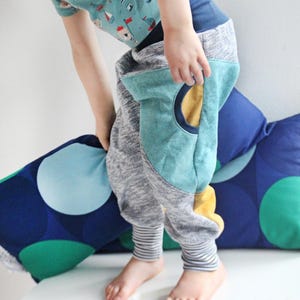 May include: A child's outfit featuring gray sweatpants with teal knee patches and striped cuffs. The outfit includes a light blue t-shirt with a nautical print. The text "Schlottis neue Kleider" is visible.