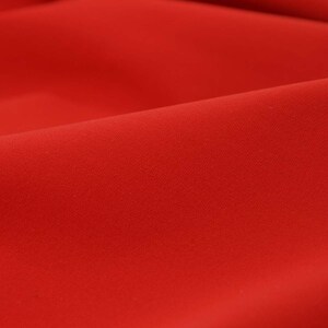 Può includere: Un primo piano di un tessuto liscio di colore rosso con una texture sottile. Il tessuto è drappeggiato e piegato, creando curve morbide e ombre.