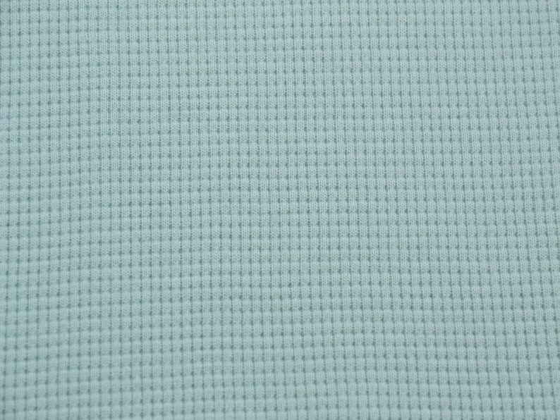 May include: A close-up of a light blue waffle knit fabric. The fabric has a textured, waffle-like pattern.