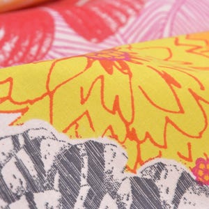 May include: Close-up of a yellow fabric with a floral pattern. The flowers are outlined in orange and have a pink center. The fabric has a white background with a gray and white striped pattern.