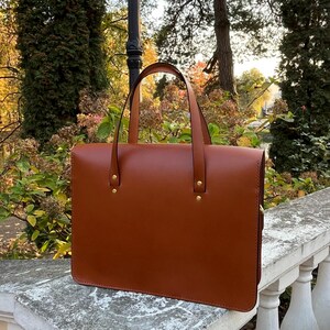 May include: A brown leather briefcase with two gold metal clasps and a top handle.