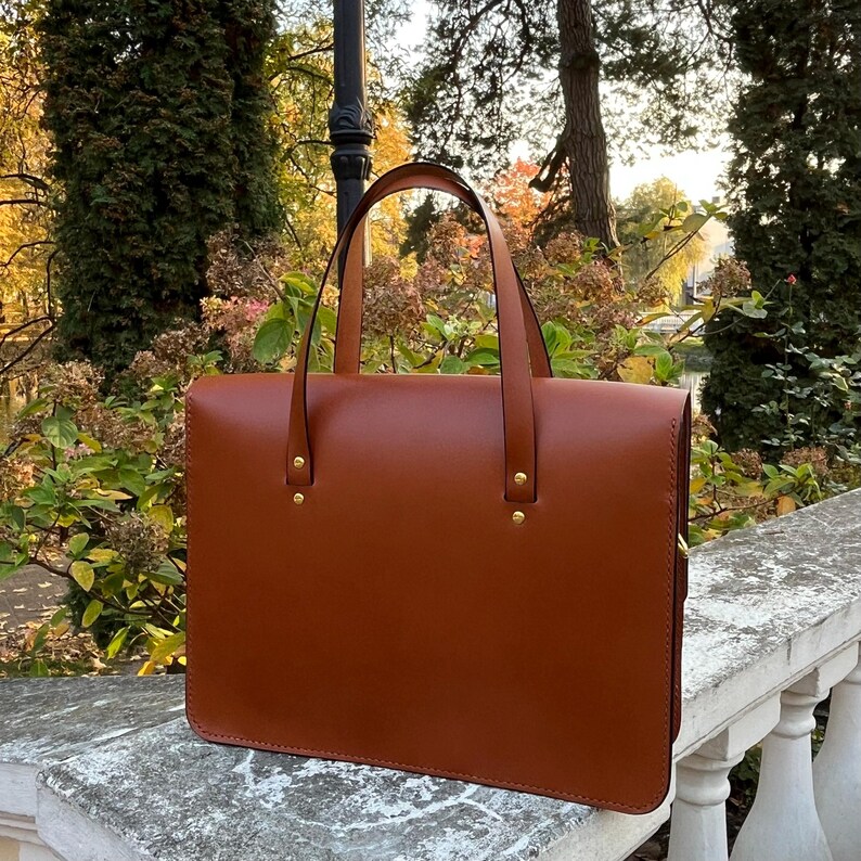May include: A brown leather briefcase with two gold metal clasps and a top handle.