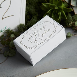 May include: A white box with a gold geometric design and the text "A Piece of Cake" in black script.