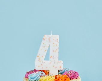 以下が含まれることがあります： カラフルなフロスティングと数字の4の形をした白いろうそくがついた白いバースデーケーキです。