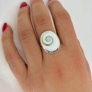 May include: A silver ring with a white oval shell cameo featuring a spiral pattern.