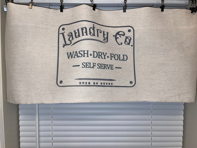 May include: A beige fabric valance with a black sign that reads "Laundry Co. Wash. Dry. Fold - Self Serve - Open 24 Hours".