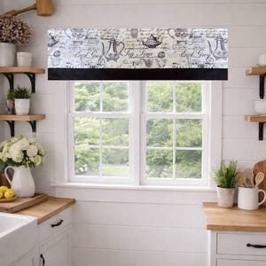 May include: A kitchen window valance with a black lower border and a cream-coloured top featuring a vintage tea-themed design. The design includes teapots, cups, and script text. The valance is mounted above a double-hung window.