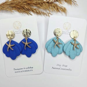 Peut inclure: Boucles d'oreilles en forme de coquillage, bleu foncé et bleu clair, avec des étoiles de mer dorées. Elles sont présentées sur des cartes blanches. Le texte 'auroracreation.eu' est visible.