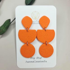 May include: Orange geometric earrings with a textured surface. The earrings are made of three connected shapes: a diamond, a half-circle, and a circle. The earrings are displayed on a white card with the text "Etsy Shop AuroraCreationEu".