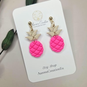 Könnte beinhalten: Handgefertigte Ohrringe mit einem Design aus hellrosa Ananas und beigefarbenen Blättern. Sie werden auf einer weißen Karte mit dem Text "Etsy Shop AuroraCreationEu" präsentiert. Die Ohrringe haben goldfarbene Kugelstecker.
