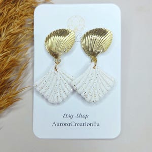 Op de afbeelding: Een paar goud-witte oorbellen in de vorm van een zeeschelp. De oorbellen hebben een gouden, geribbelde bovenkant en een witte, waaiervormige onderkant met gouden spikkels. De tekst "Etsy Shop AuroraCreationEu" is zichtbaar.