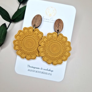 Könnte beinhalten: Ein Paar senfgelbe Hängeohrringe mit einem detaillierten Mandala-Design. Die Ohrringe sind aus Polymer Clay gefertigt und haben Holzakzente. Die Ohrringe sind auf einer weißen Karte mit dem Text "Instagram & webshop auroracreation.eu" abgebildet.