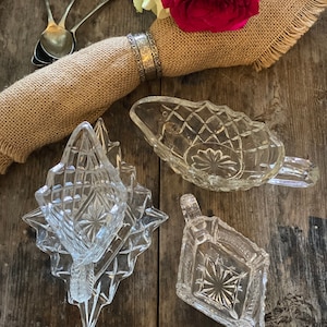 May include: Three clear glass dishes with a cut glass design. The dishes are on a wooden surface with a hessian napkin and a bouquet of roses.